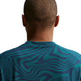 Person wearing a teal and navy patterned shirt on a white background