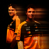 Two men wearing orange and black PUMA McLaren replica jerseys with various sponsor logos