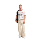 A man modeling a white Puma AC Milan FC Bellerose jersey with 'Emirates FLYBOOST' sponsor text, paired with beige wide-leg trousers and white sneakers, on a solid white background.