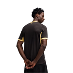 A man shown from the back wearing a dark brown short-sleeve athletic jersey with gold/yellow contrast panels on the shoulders and sides, against a plain white background.