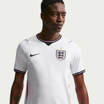 Person wearing a white sports jersey with a logo on a light gray background