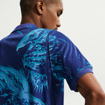 Man wearing a blue polo shirt with a tiger design on the back against a light gray background