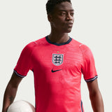 Person wearing a red soccer jersey with a logo, holding a soccer ball on a light background