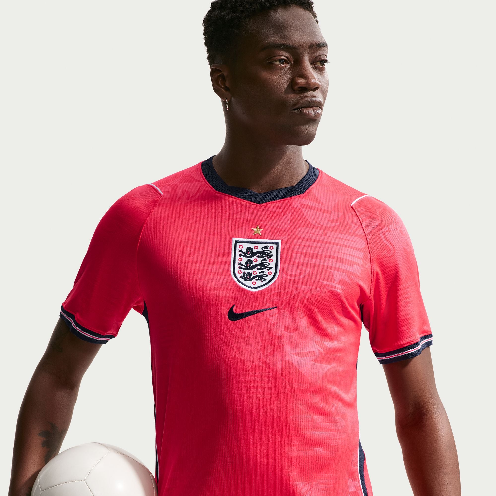Person wearing a red soccer jersey with a logo, holding a soccer ball on a light background
