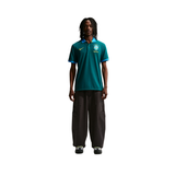 Person wearing a teal sports jersey with a logo on a white background