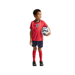 Child wearing a red soccer jersey and shorts holding a soccer ball on a white background