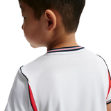 Child wearing a white sports jersey with red and blue accents on a white background