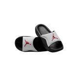 A pair of black and white slide sandals featuring the red Jumpman logo on the straps, displayed against a solid white background.
