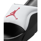 A close-up of a slide sandal featuring a white upper with a red Jumpman logo, a black textured footbed, and a black sole.