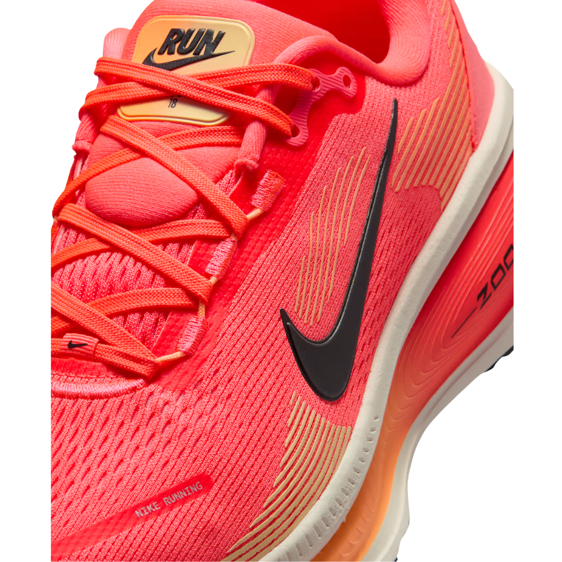 A close-up of a Nike running shoe in bright coral pink and orange, featuring a black Swoosh logo, orange laces, and a white midsole.