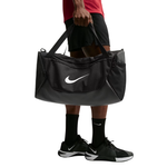 A person holding a large black Nike duffel bag with a white swoosh logo, wearing black athletic shorts, socks, and sneakers against a plain white background.