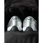 A pair of silver Nike F50 tennis shoes with black and white soles, nestled inside a black backpack.