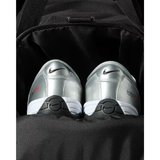A pair of silver Nike F50 tennis shoes with black and white soles, nestled inside a black backpack.