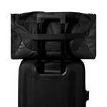 A black duffel bag with an extended telescoping handle resting on top of a black rolling suitcase against a plain white background.