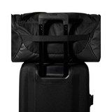 A black duffel bag with an extended telescoping handle resting on top of a black rolling suitcase against a plain white background.