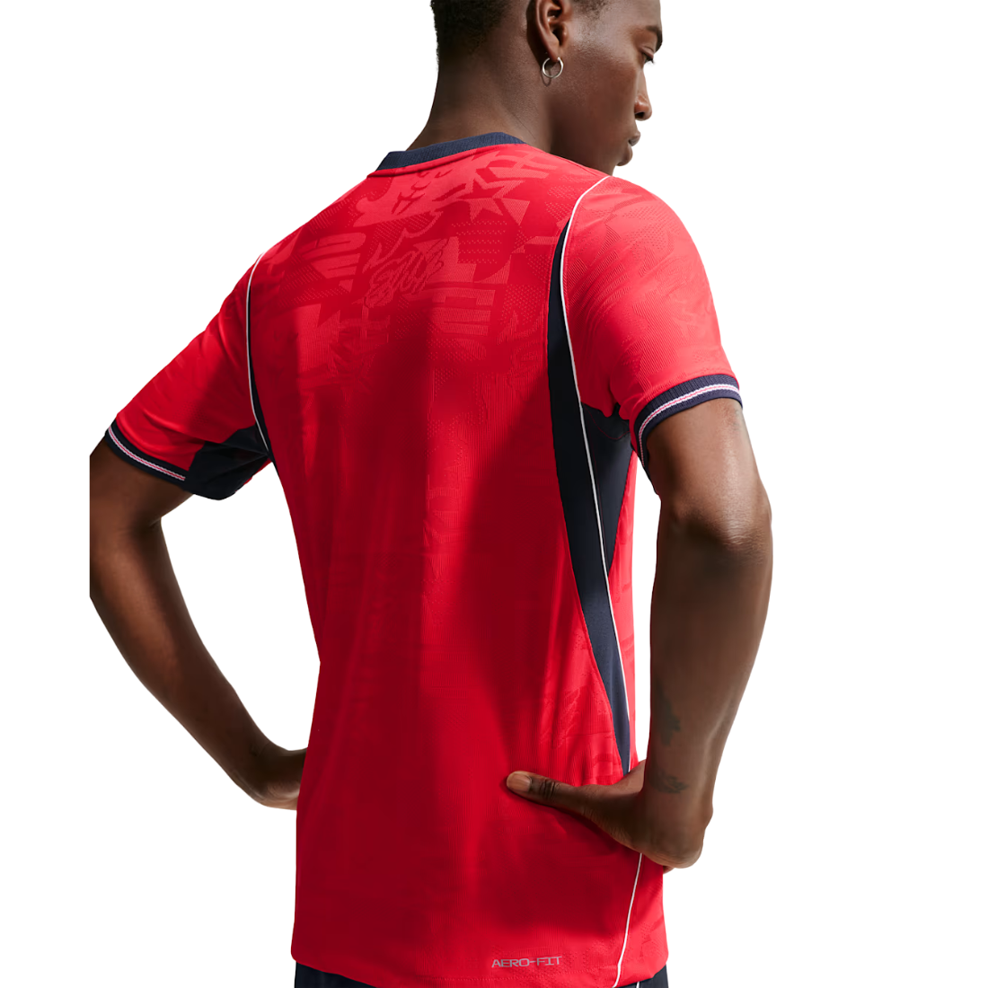 A man wearing a red short-sleeve athletic jersey, shown from the back. The jersey features navy blue and white side panels, navy blue collar trim, and a subtle tonal graphic pattern on the upper back.