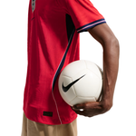A close-up of a person wearing a red Nike soccer jersey and holding a white soccer ball against a clean white background.