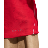 Close-up of a red athletic top with a perforated fabric panel and the text 'AEROFIT' near the hem, shown against a white background with beige fabric underneath.
