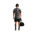 A man shown from the back wearing a gray and black camouflage short-sleeve athletic t-shirt, black shorts, black socks, and gray sneakers, while holding a black duffel bag against a plain white background.