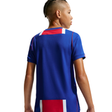 A child wearing a royal blue athletic jersey, shown from the back and side profile against a plain white background.