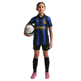 A young girl modeling an Inter Milan soccer jersey, shorts, and socks, holding a soccer ball against a plain white background.