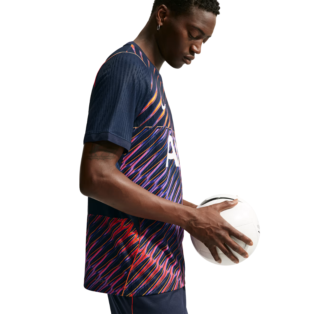 A man wearing a navy blue soccer jersey with a vibrant diagonal multicolor stripe pattern in red, pink, orange, and purple, holding a white soccer ball against a solid white background.