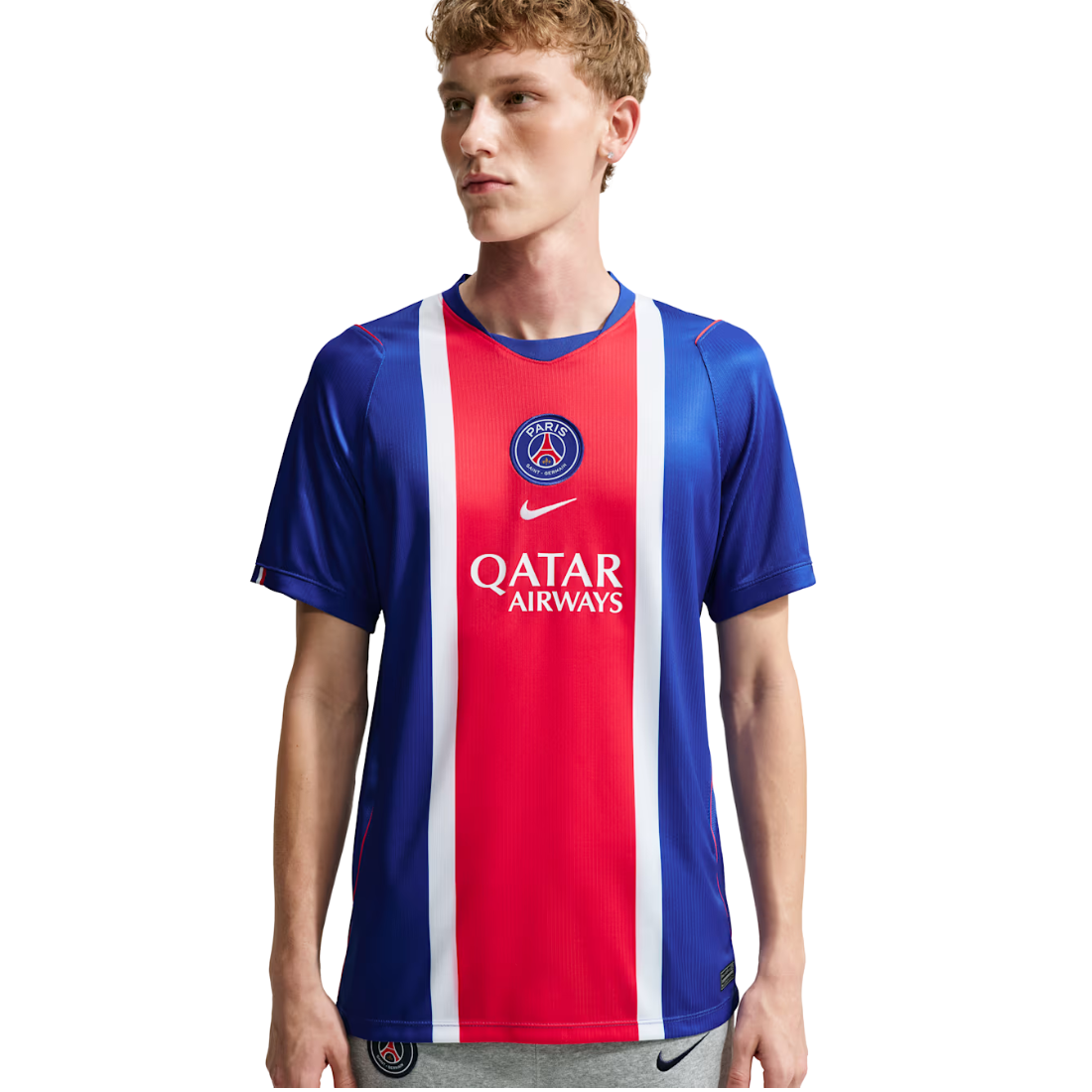 A young male model wearing a Paris Saint-Germain Nike soccer jersey with a red, white, and blue vertical stripe design, featuring the Paris Saint-Germain crest and Qatar Airways sponsor logo.