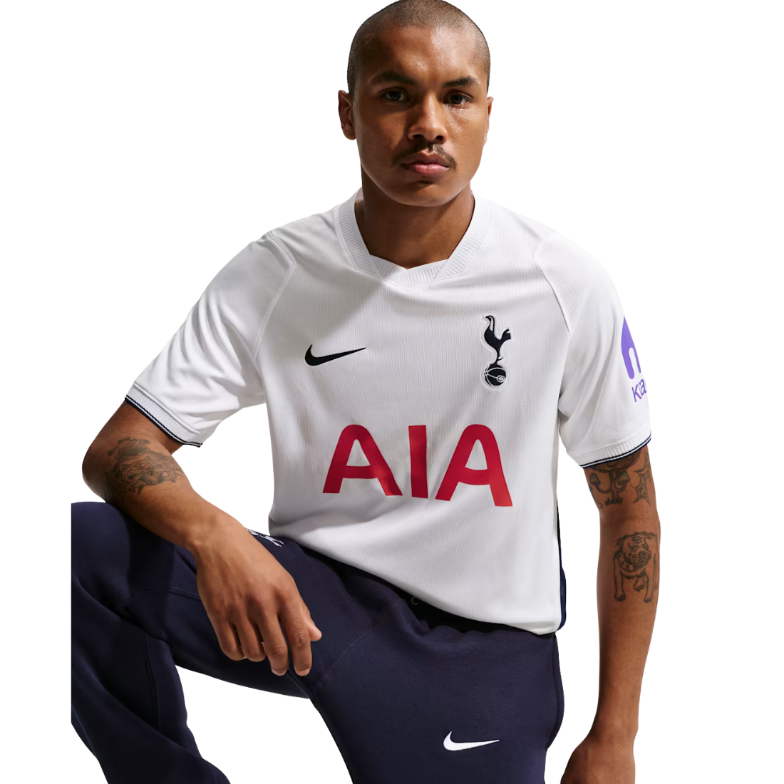A man wearing a white Tottenham Hotspur football jersey with navy blue trousers, posed against a solid white background.