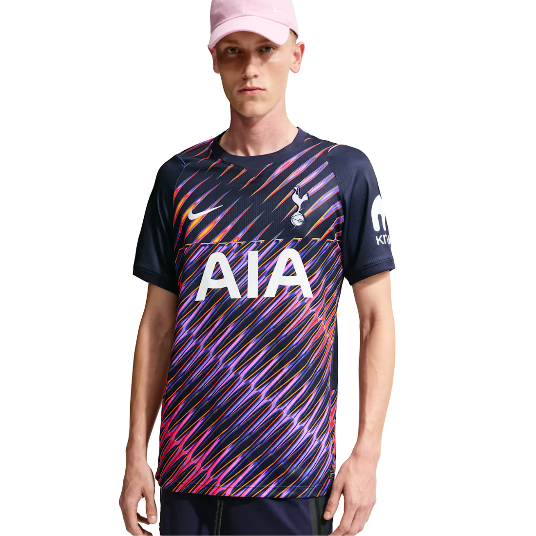 A man wearing a dark navy Tottenham Hotspur soccer jersey with a vibrant pink, purple, and orange diagonal striped pattern, paired with a pink cap, against a plain white background.