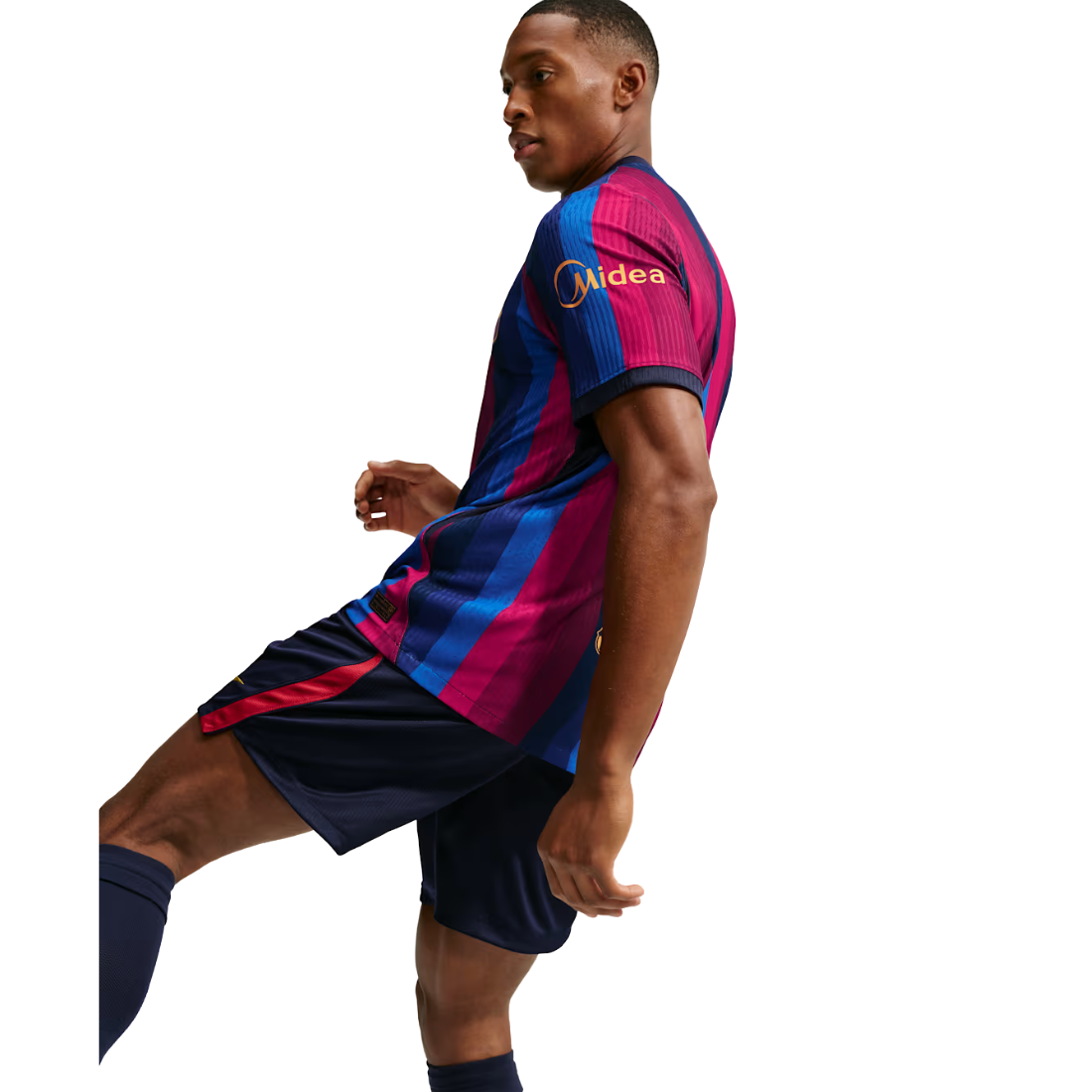 A man modeling a FC Barcelona home soccer jersey and shorts kit against a solid white background. The jersey features the classic blue and magenta vertical stripes with a gold Midea logo on the right chest, paired with dark navy blue shorts.