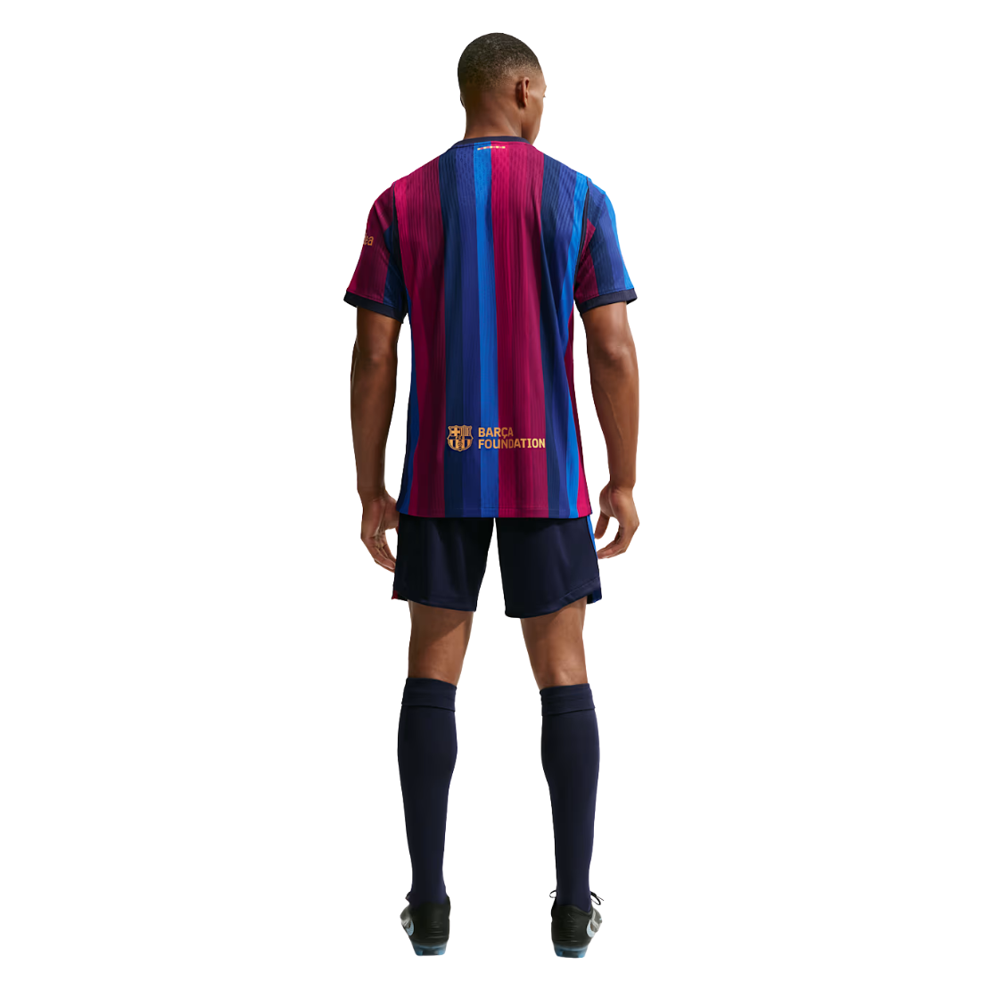 A man viewed from the back wearing a short-sleeve soccer jersey with vertical blue, magenta, and navy stripes, navy shorts, and navy knee-high socks on a white background.