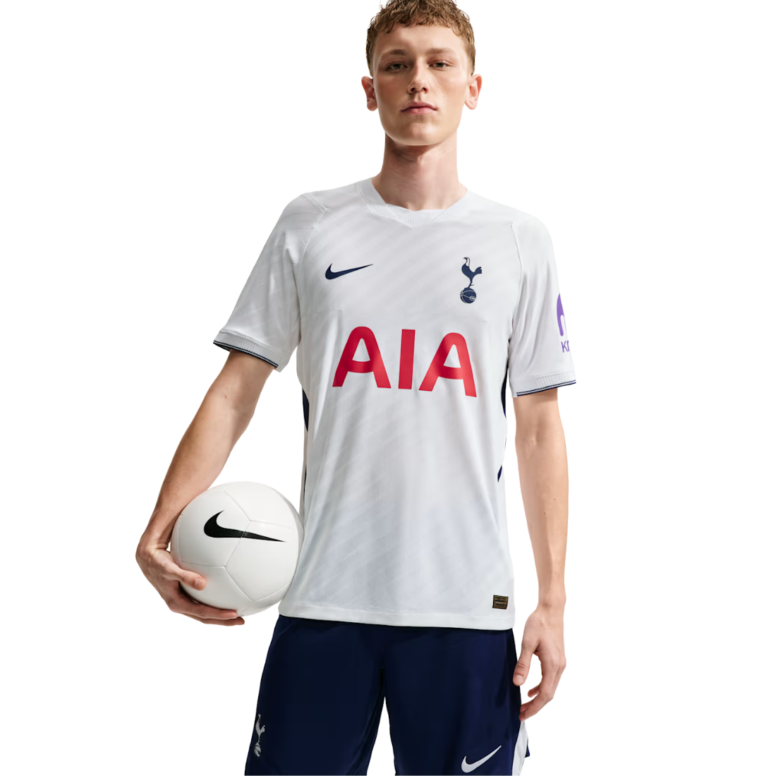 A young male model wearing a white Nike Tottenham Hotspur football jersey with red AIA sponsor text, holding a white soccer ball against a plain white background.