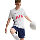 A man wearing a white Tottenham Hotspur soccer jersey with navy shorts and white socks, posed with a white soccer ball against a solid white background.
