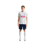 A male model wearing a white Tottenham Hotspur soccer jersey with red AIA sponsor logo, navy shorts, white socks, and white shoes, photographed against a plain white background.