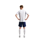 A man shown from the back wearing a white short-sleeve athletic jersey with dark navy side panels, matching navy shorts, white knee-high socks, and white cleats, isolated on a light gray background.