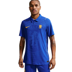 A man modeling a blue Chelsea football jersey with yellow Nike and club crest details, paired with matching blue shorts, against a plain white background.