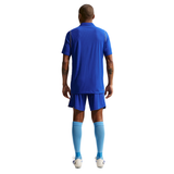 A man shown from the back wearing a royal blue soccer kit consisting of a short-sleeve jersey, matching shorts, light blue knee-high socks, and white soccer cleats, isolated on a white background.