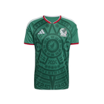 Green Mexico national football team jersey with a dark green Aztec calendar pattern, featuring the white Adidas logo and Mexican crest on the chest, set against a plain white background.