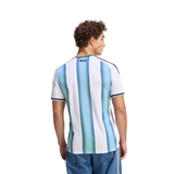 A man viewed from the back wearing a short-sleeve Argentina-style striped jersey with vertical light blue, medium blue, and white stripes, plus dark trim at the collar and sleeve cuffs. The number 1933 is printed near the back neckline.