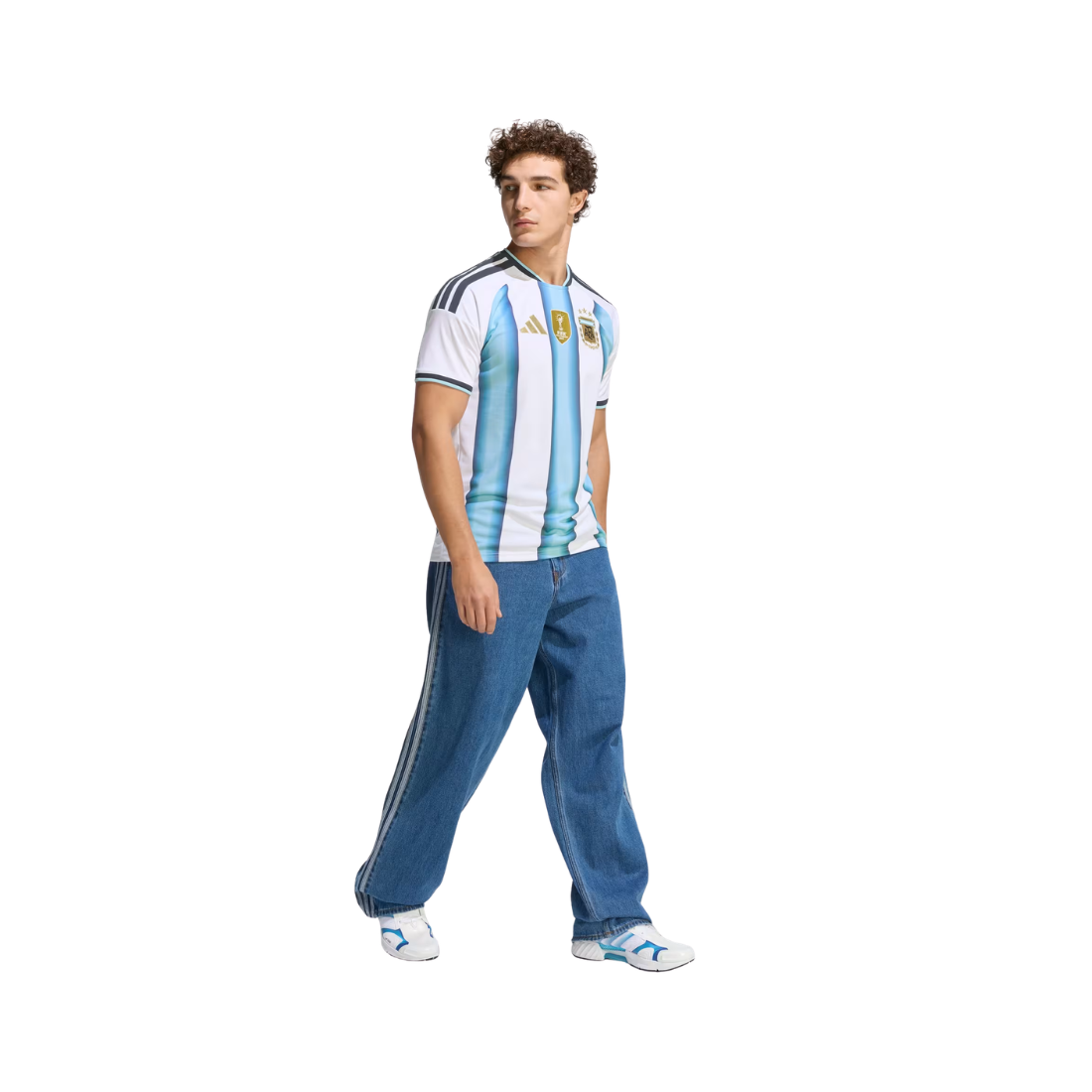A man modeling a vintage-style Argentina national football team jersey with light blue and white vertical stripes, paired with blue jeans and white sneakers, against a plain white background.