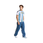A man modeling a vintage-style Argentina national football team jersey with light blue and white vertical stripes, paired with blue jeans and white sneakers, against a plain white background.