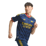 A male athlete wearing a navy blue Arsenal soccer jersey with yellow and red accents, featuring the Adidas logo and Emirates Fly Better sponsor text, set against a plain white background.