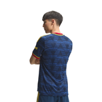 A man wearing a dark blue patterned soccer jersey with yellow and red trim, shown from the back against a plain white background.