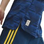 Close-up of a blue Adidas athletic top with a subtle geometric pattern, featuring a gold and white Adidas Originals patch on the sleeve and yellow stripes on the matching shorts.