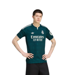 A male model wearing a dark teal Real Madrid home soccer jersey with white Adidas and Emirates branding, paired with black shorts, against a solid white background.