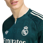 Close-up of a person wearing a dark green Real Madrid soccer jersey with white accents, including the club crest, Adidas logo, and three stripes on the shoulder.