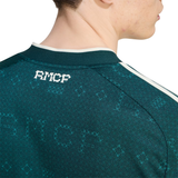 Close-up of the back of a dark teal patterned sports jersey with a white 'RMCF' logo on the neck, worn by a model.