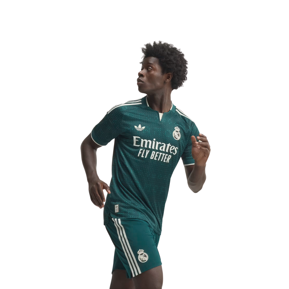 A man wearing a dark green Real Madrid soccer jersey and matching shorts with white stripes, posed against a solid white background.