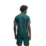 A man viewed from behind wearing a dark green patterned soccer jersey and matching shorts against a plain white background.