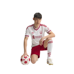 A male soccer player kneeling on a white background, wearing a white and red Liverpool FC jersey, matching shorts, white socks, and soccer cleats, while holding a red and white soccer ball.
